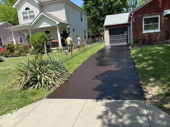 The same older driveway after crack filling and seal coating, dark and uniform to the garage