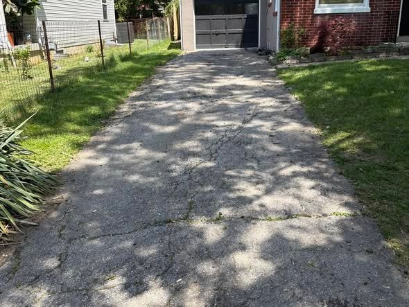 Older narrow driveway with wide cracks and weeds growing through before repair